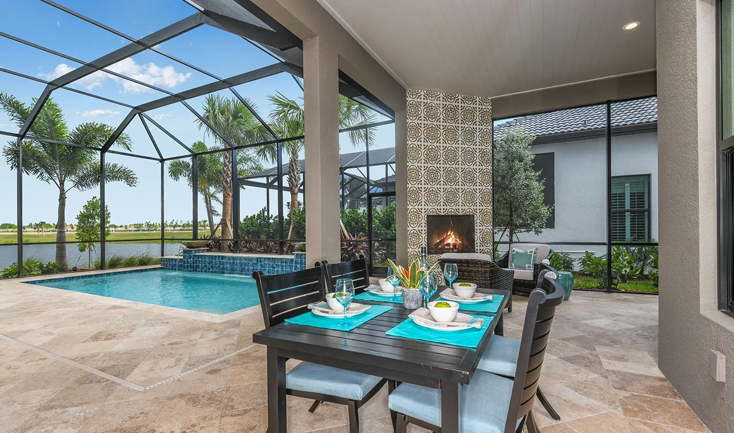Covered lanai with pool, outdoor dining, and fireplace in a Neal Signature home